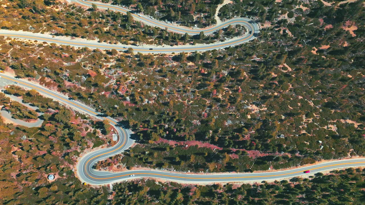 Mountainous landscape crossed by the twisted road. Sunny day footage over the wooded territory from aerial perspective.