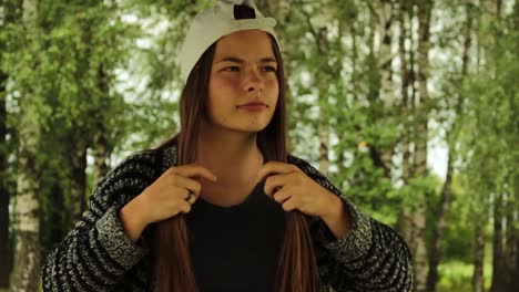 Girl-putting-on-a-white-hat,-doing-her-hair-in-the-nature