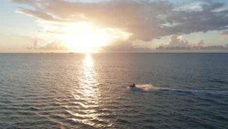 lado aéreo de seguimiento de vuelta iluminado jet-ski con un par de jinetes montar a toda velocidad con el atardecer sobre el horizonte