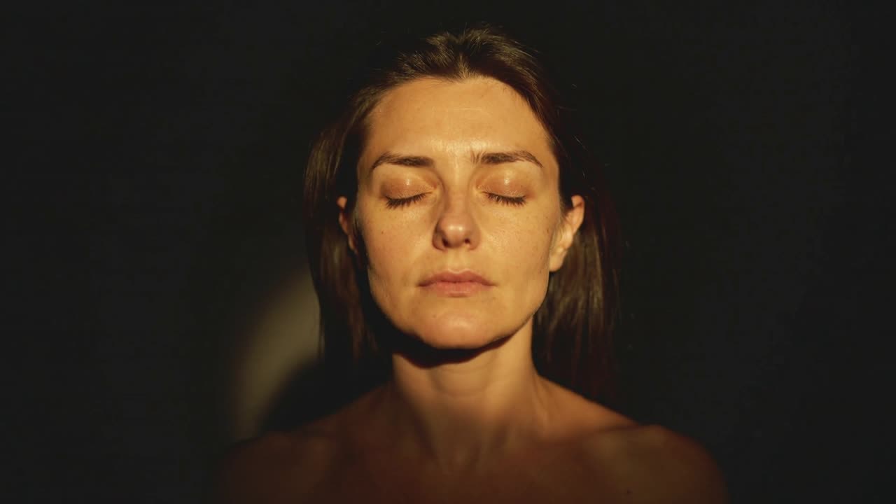 Moving warm light beam crossing woman face in studio, revealing exposed shoulders and contours