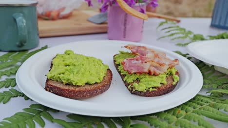 slow motion close up, crispy bacon placed on avocado toast during forest brunch