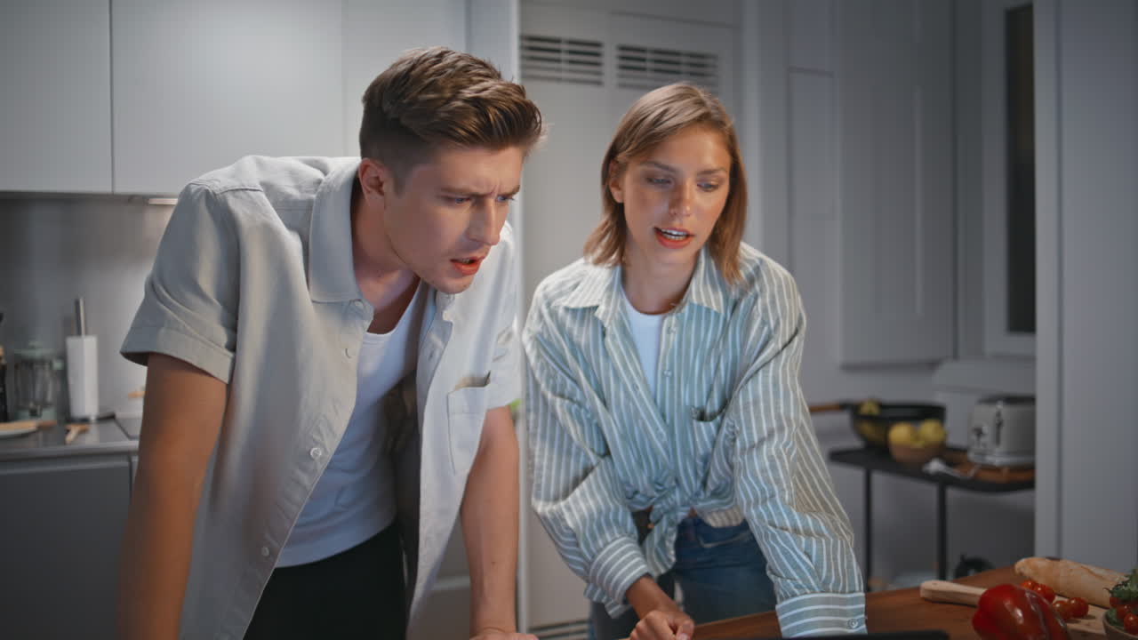 Young family preparing dinner in evening together. Relaxed couple watch laptop