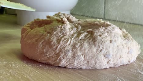mujer rociando harina sobre masa fresca en la mesa de la cocina