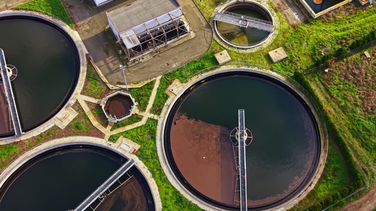 Wastewater treatment facility showcases circular tanks under clear blue sky surrounded by green fields during a sunny day