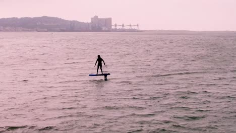 aerial tracking of sportsman falls while practicing hydrofoil on the tagus river, with caparica in the background in cloudy day