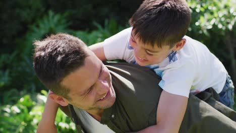 Portrait-of-caucasian-father-carrying-son-on-his-back-in-the-garden