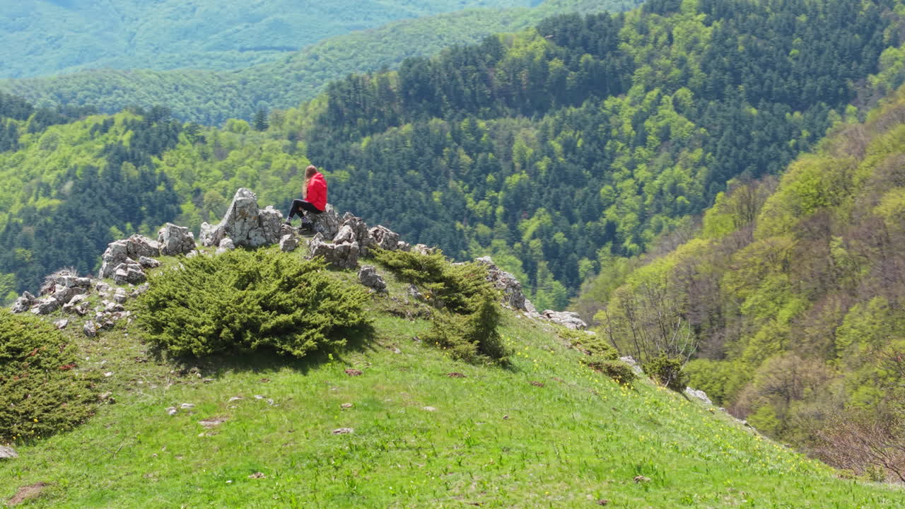 Aerial view of a lone woman hiker gazing into the vast green wilderness from an elevated spot. A peaceful outdoor escape in the heart of Bulgaria’s scenic mountains.