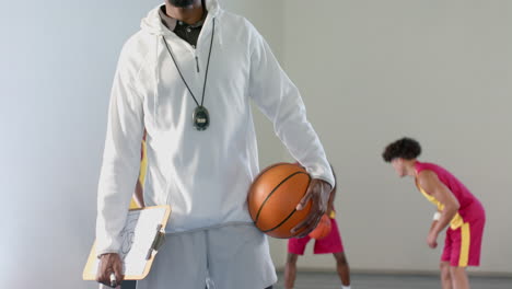 Entrenador-Afroamericano-Sostiene-Una-Pelota-De-Baloncesto-En-Un-Gimnasio