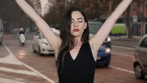 Young-beautiful-caucasian-brunette-woman-wearing-boxing-wraps-stretches-arms-and-punches-toward-camera-with-traffic-timelapse-in-background