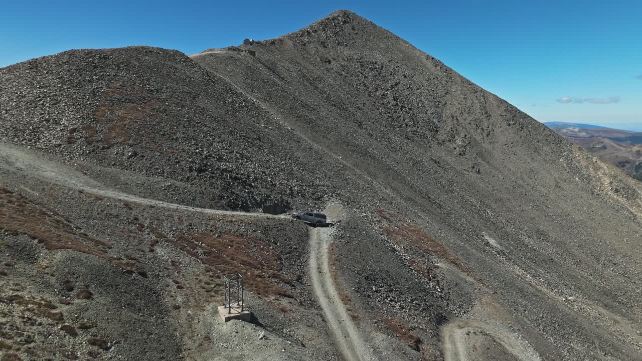Aerial orbit to rearview of offroad car driving up sharp hairpin turn on technical mountain trail in Colorado