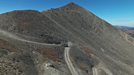 aerial orbit to rearview of offroad car driving up sharp hairpin turn on technical mountain trail in colorado