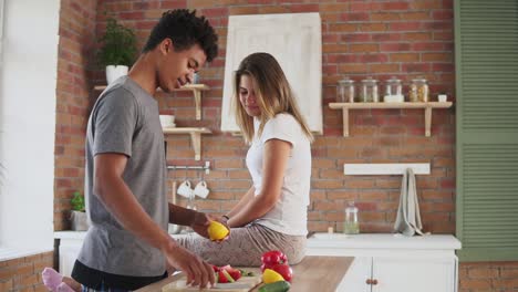 handsome african guy preparing salad, cutting lemon and squeezing juice from it in a funny way while his caucasian girlfriend is