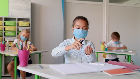 little girl with face mask in class puts hand sanitizer on her hands. covid-19 pandemic. children back to school after coronavirus lockdown.