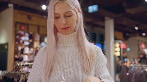 medium shot of female buyer holding brown rain coat by hanger examining fabric texture in modern boutique with clothing racks in background evoking refined shopping moment