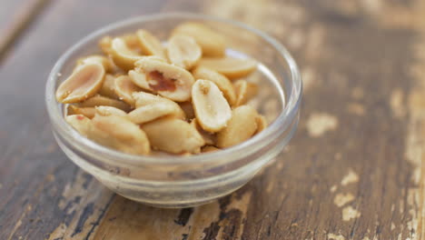 close up view of roasted salted peanuts in the glass bowl on the wooden old table