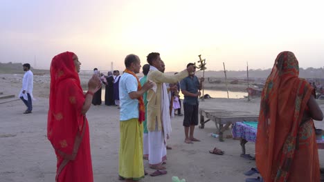 hindu devotees performing rituals on the ganges river bank at sunset in varanasi, india
