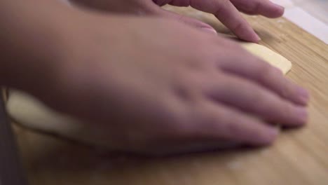 manos volteando un disco delgado de masa sobre una superficie de madera enharinada, cerrar