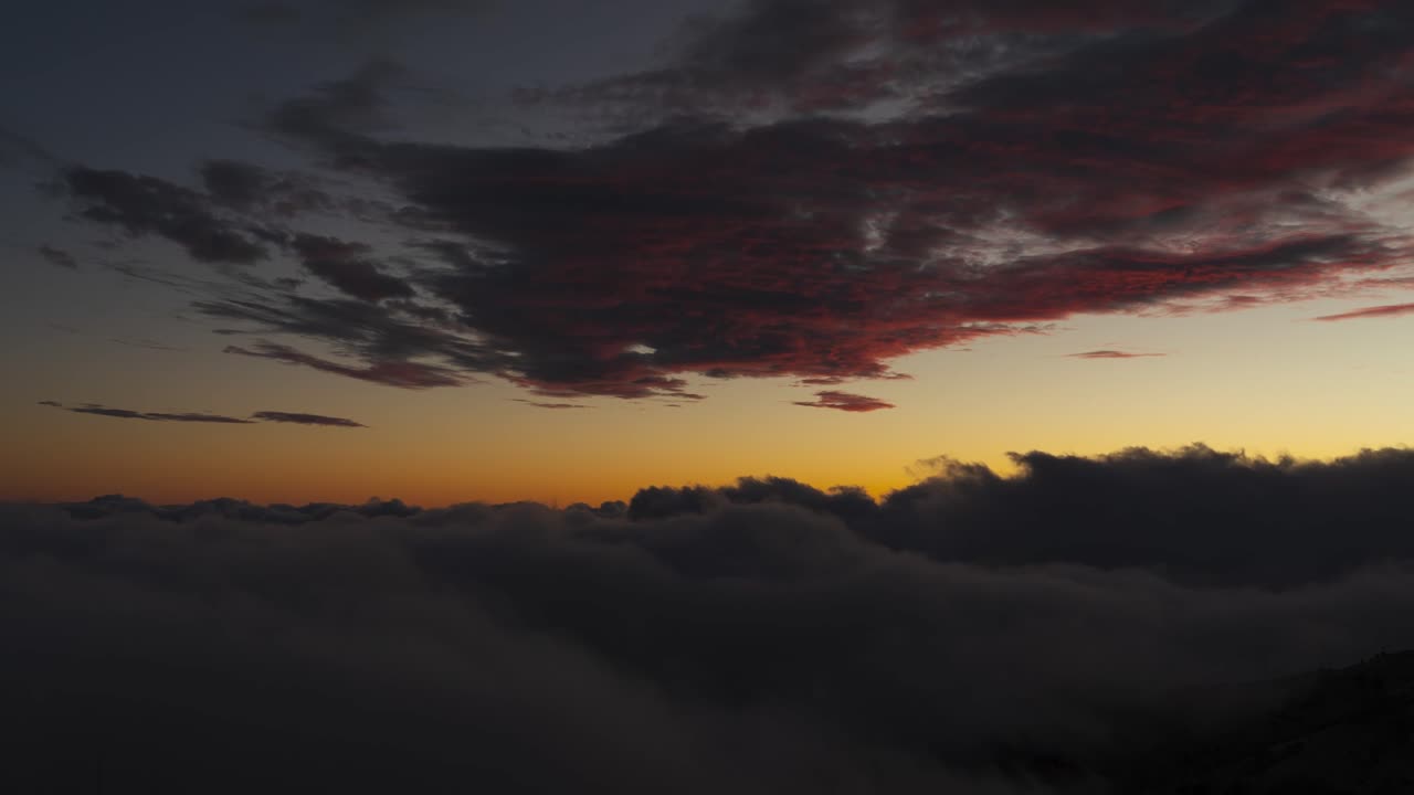Sunlight coloring clouds above sea of mist rolling over mountains in Madeira, timelapse