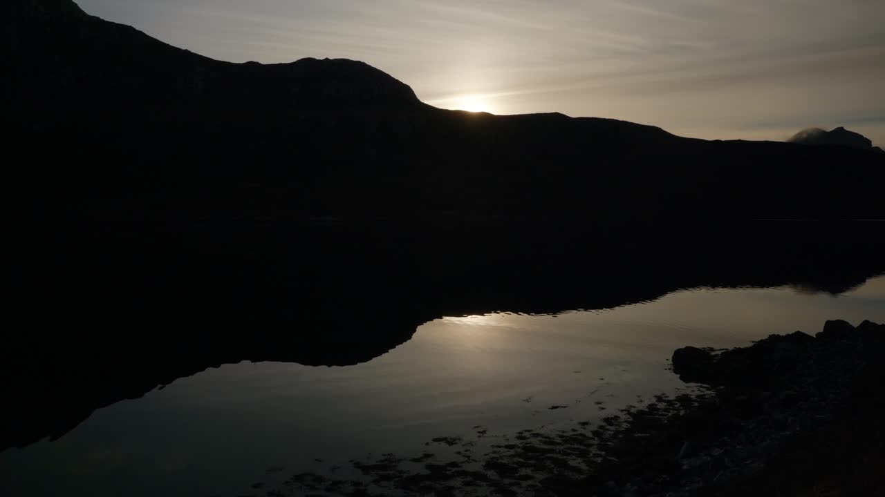 Vuoren varjo heijastuu täydellisesti Skotlannin merenlahden veteen auringonlaskun aikaan, samalla kun aallot liikkuvat lempeästi veden pinnalla.