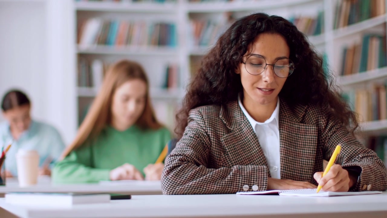 Giovane donna che scrive su un quaderno alla scrivania in biblioteca