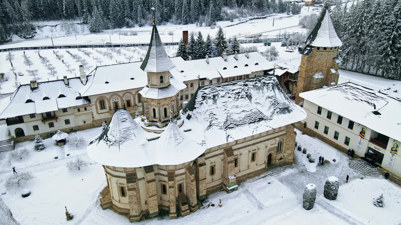 Lotniczy widok z drona na monastyr Putna zimą, Rumunia. Wewnętrzny dziedziniec z przechadzającymi się turystami, nagie drzewa, śnieg, wzgórza wokół