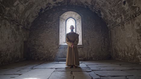 monk standing in an ancient chapel with weathered stone walls, sunlight streaming through a window, creating a serene and spiritual atmosphere perfect for deep prayer and contemplation