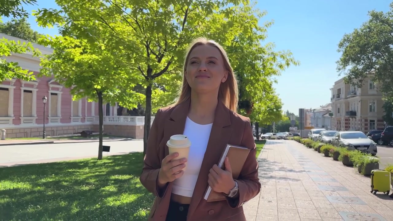 Giovane donna professionista che cammina e beve caffè per strada in città