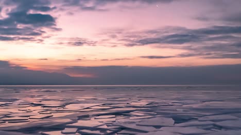 Rafted-ice-on-a-frozen-lake,-mountains-and-cloudscape---time-lapse-zoom-out