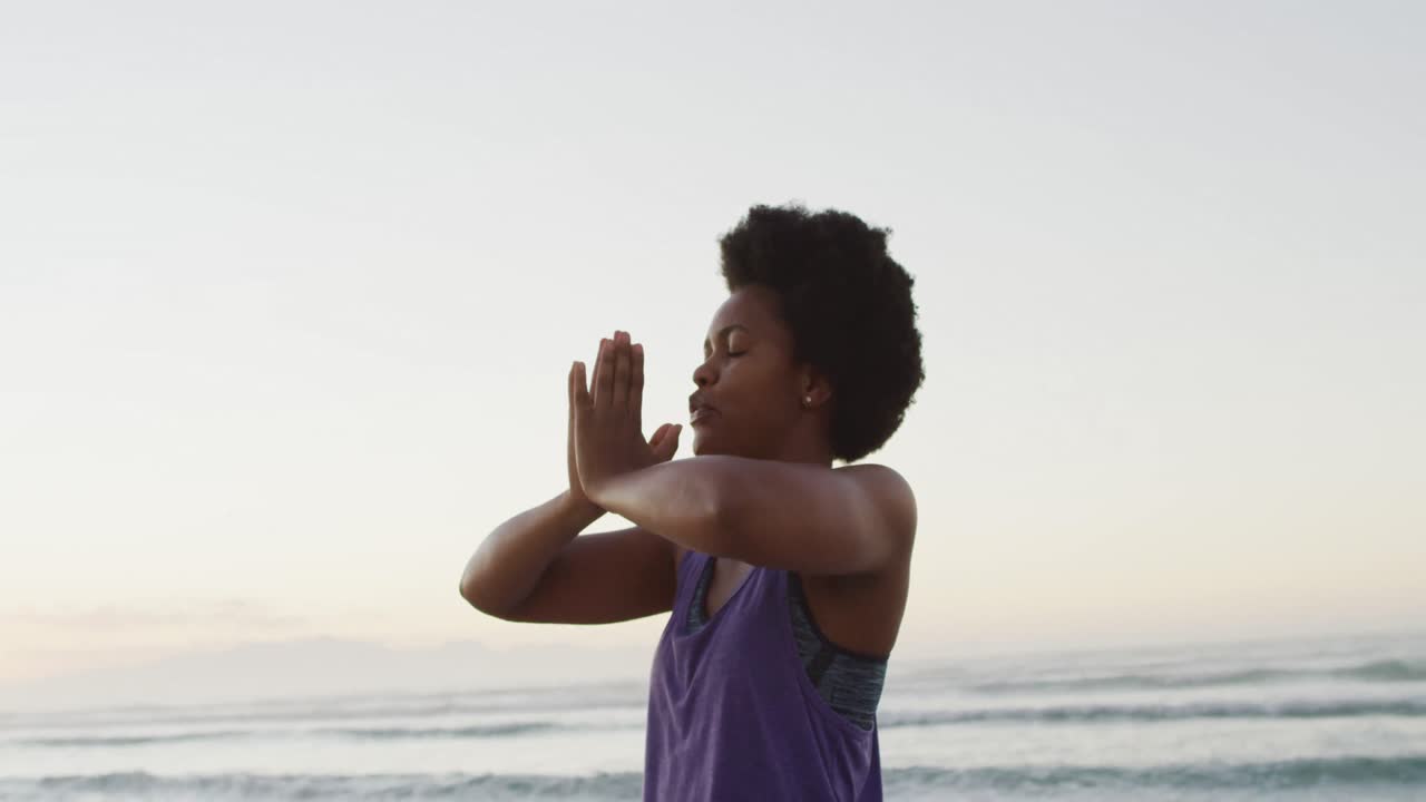 African american woman practicing yoga and meditating on sunny beach