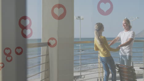múltiples iconos de corazón rojo flotando contra una pareja caucásica bailando en el balcón