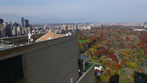 Fliegen-Sie-Um-Die-Spitze-Des-Hochhauses-Herum.-Aufschlussreicher-Panoramablick-Auf-Den-Herbstlichen-Central-Park,-Umgeben-Von-Hohen-Gebäuden.-Manhattan,-New-York-City,-Vereinigte-Staaten