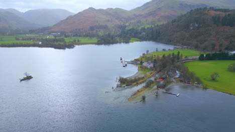 Approaching-drone-shot-of-the-scenic-view-of-mountains,-fields-and-lakeside-of-Ullswater,-showing-some-boats-docked-by-the-lake-in-a-countryside-village-in-England,-in-United-Kingdom