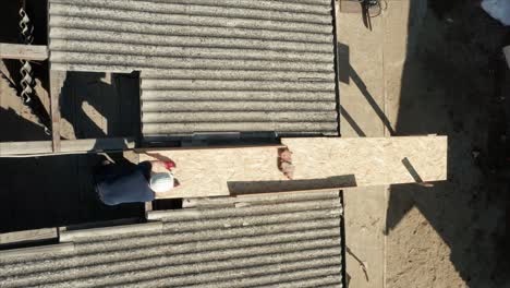 worker wearing hard hat slide debris on plywood between the hole on asbestos roof