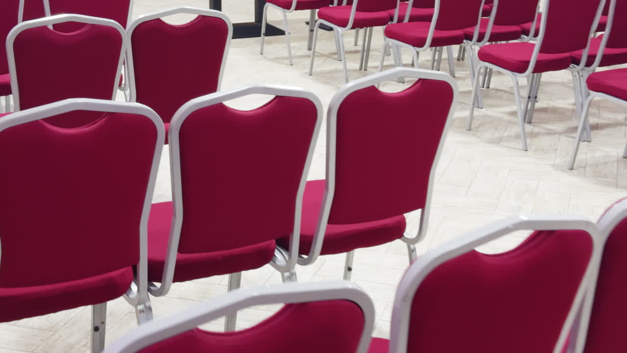 Several rows of pink chairs inside the room. Empty seats for invited guests in the ceremony space.
