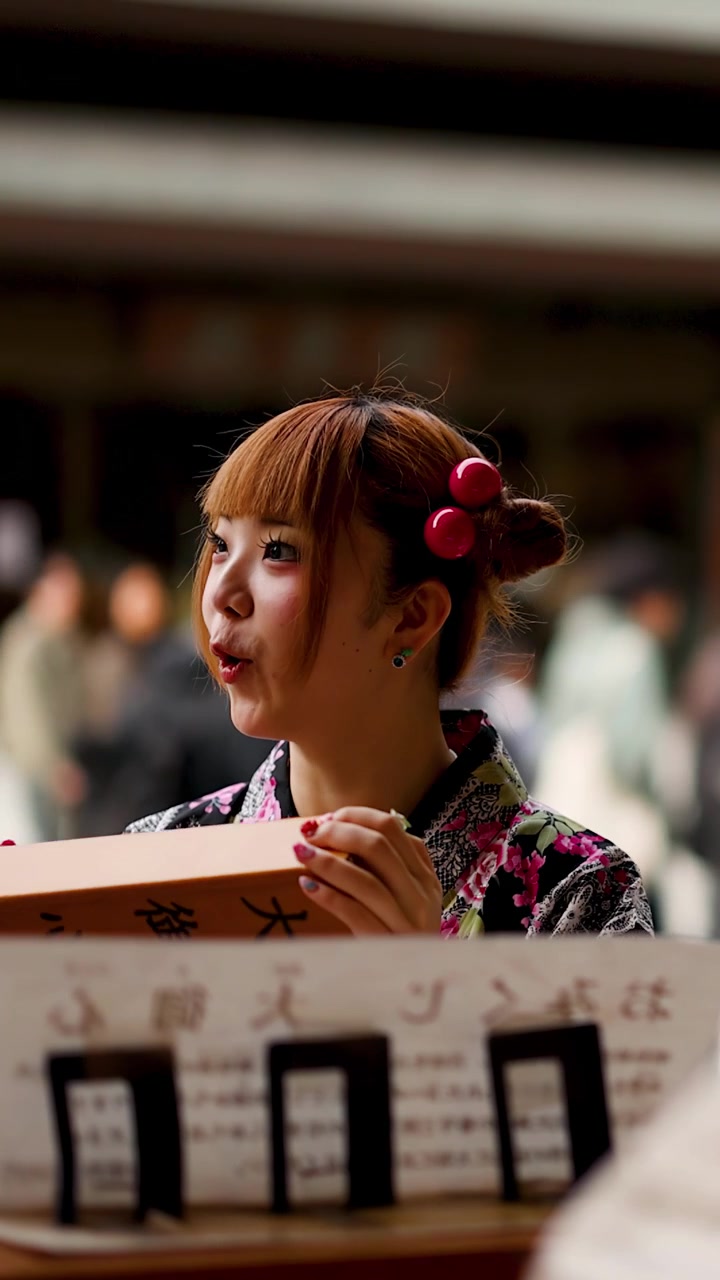 寺で伝統的な着物を着た笑顔の日本人女性が木製のおみくじ箱を振る