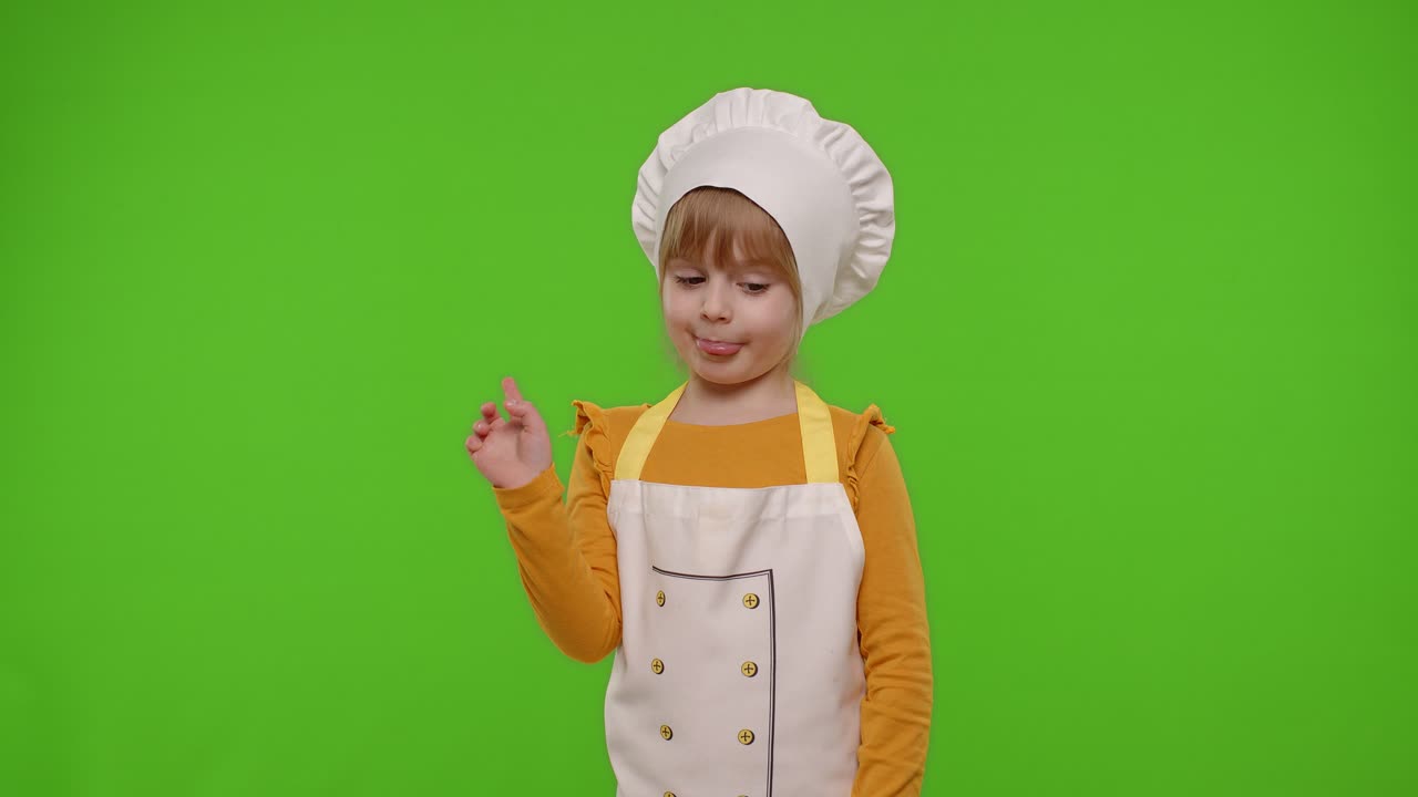 Bambina vestita da cuoca e fornaia con grembiule che balla, scherza, mostra la lingua, su sfondo chroma key.