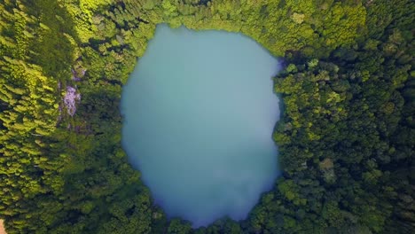 descenso de drones hacia un lago redondo de agua azul turquesa rodeado de selva tropical en una isla volcánica