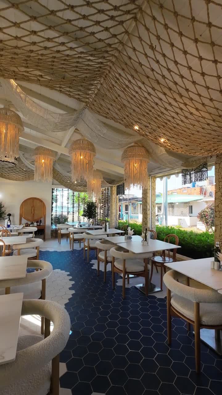 Bright and airy cafe restaurant interior with Large Windows, blue and white floor , white tables, and unique macrame hanging lights