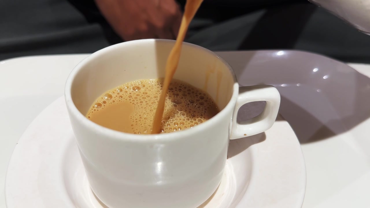 Primo piano di tè masala chai indiano appena preparato versato in una tazza di ceramica bianca, che cattura il suo colore ricco, la consistenza cremosa e la superficie schiumosa.