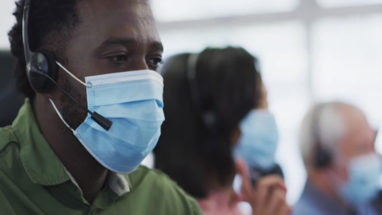 Man wearing face mask and headset talking while sitting on his desk at office