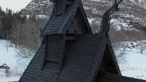 Borgund-stave-church-closeup-detail-shot-of-tower-with-ornaments-and-dragon-sculpture-carvings-in-wood---Aerial-rotating-slowly-close-around-top-of-historic-building