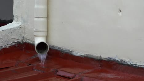 rainwater from the top gutter pours out of a residential drainage spout during a drizzle