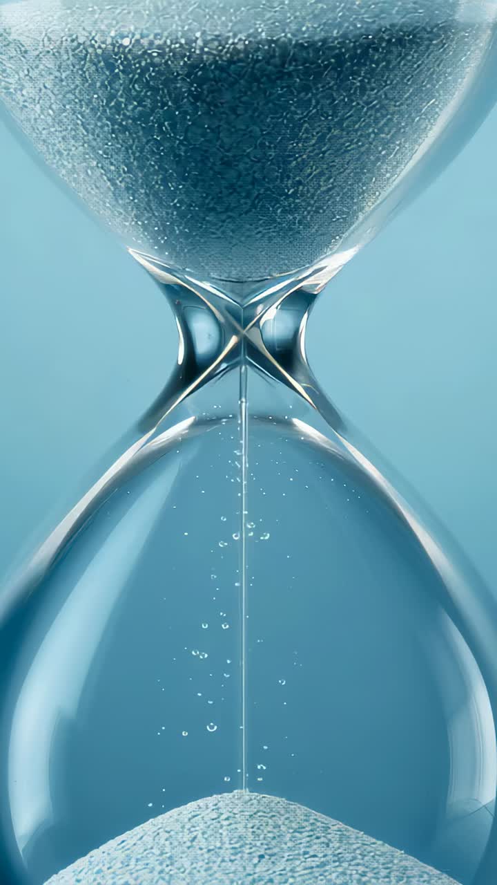 Vertical video: Gravity pulling pale sand through clear hourglass in studio, forming conical pile