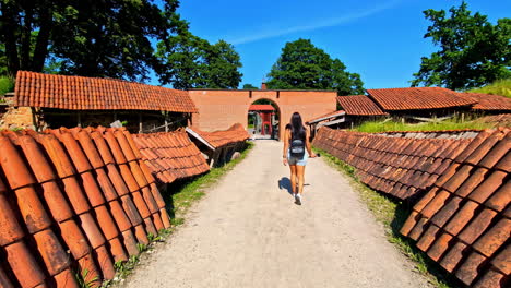 woman with backpack walking towards arched brick gateway with tiled roofs on either side of pathway during daytime