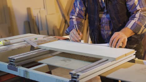 the carpenter measures the wood with the meter and marks it with a pencil.