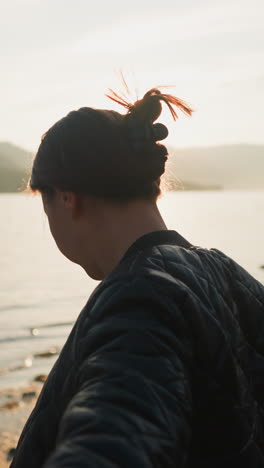 la esposa sostiene a su marido de la mano en la orilla del río al atardecer. el romance florece entre la pareja joven durante el intercambio de vacaciones entre el paisaje rural. momentos optimistas de la vida