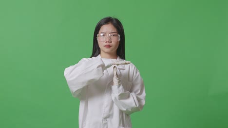 화가 난 아시아 여성 과학자는 머리를 흔들고 실험실의 녹색 스크린 배경에 서서 손으로 타임 아웃 제스처를 하고 있습니다.
