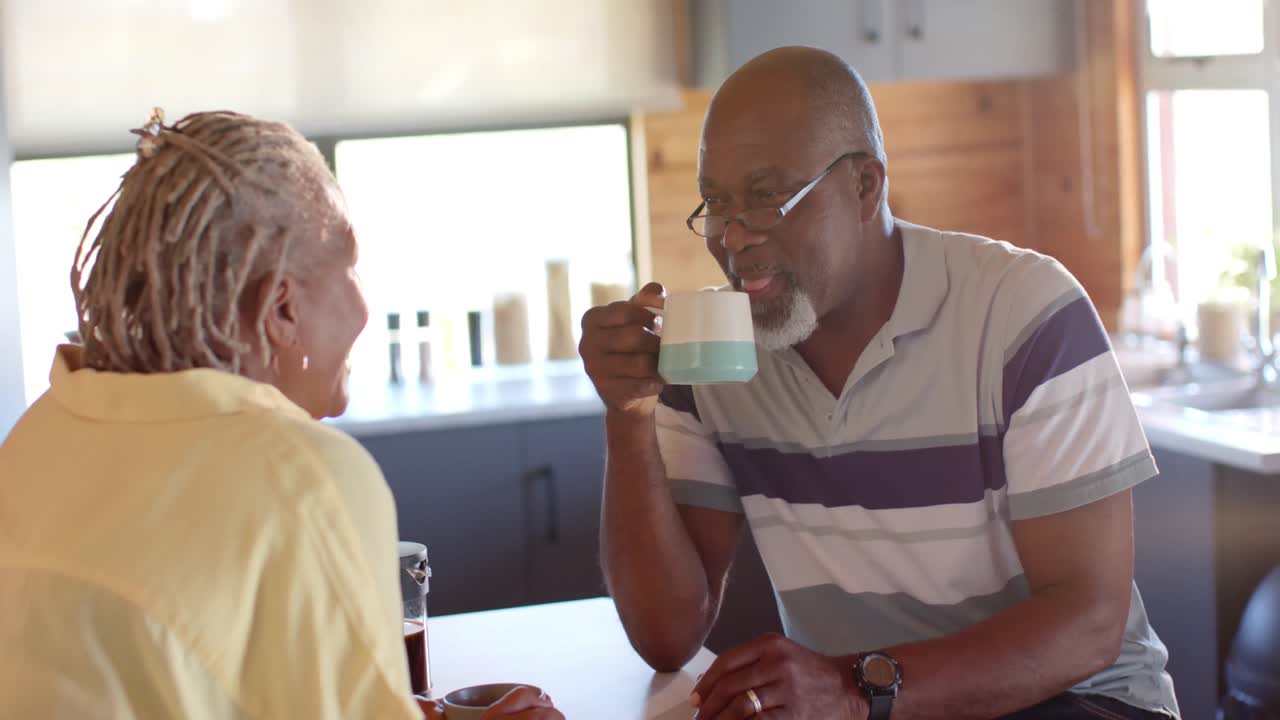 Heureux couple de seniors afro-américains buvant du café et discutant dans la cuisine, au ralenti