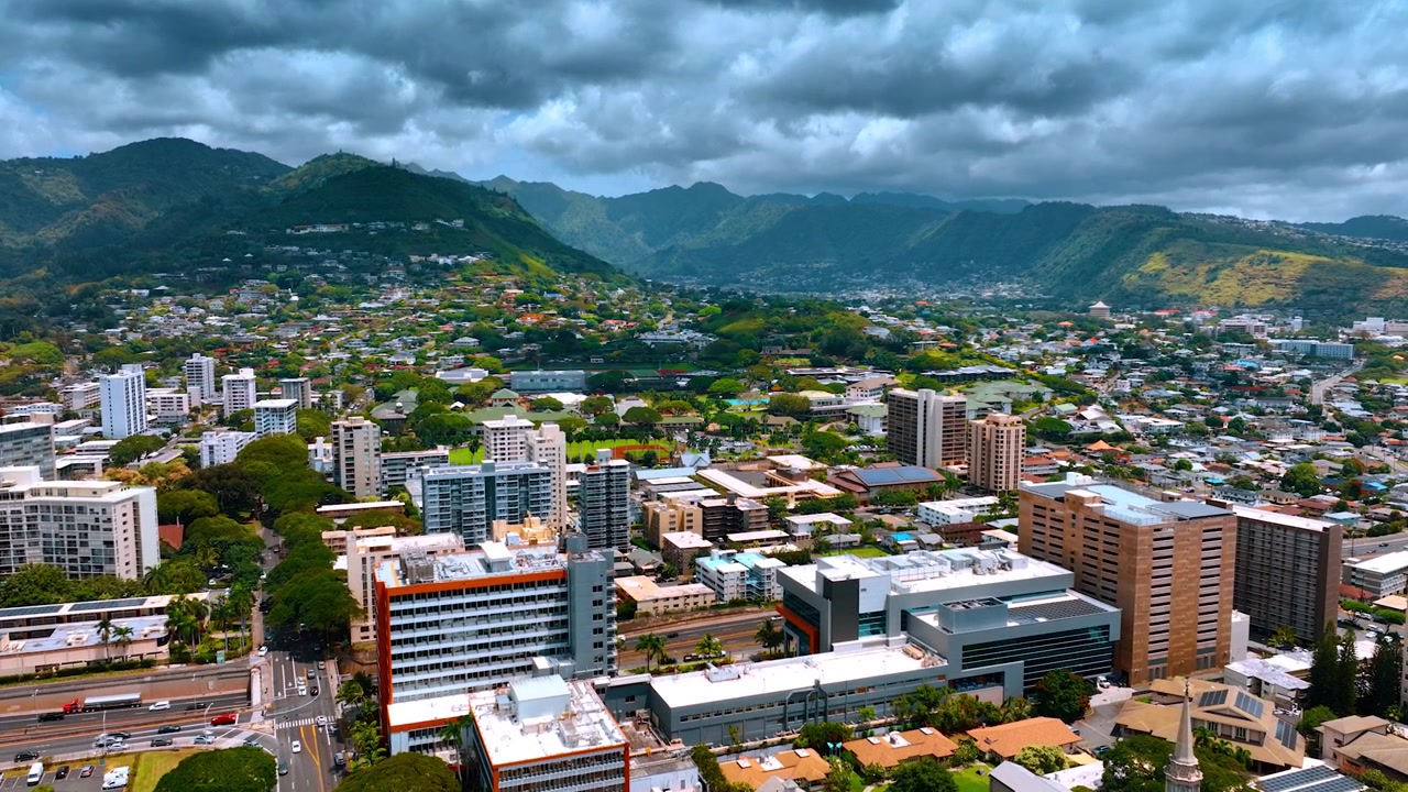 Avvicinamento alle montagne verdeggianti che circondano la vasta città. Un cielo drammatico copre la bellissima Honolulu, Hawaii, USA. Vista aerea