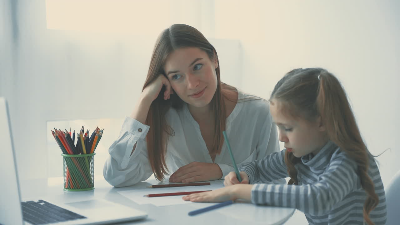 Young Woman Helps Little Girl To Do Homework Using Laptop